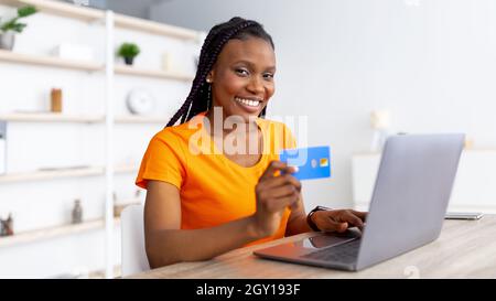 E-Commerce. Millennial African American Dame mit Kreditkarte für die Fernzahlung, Online-Shopping über Laptop zu Hause Stockfoto