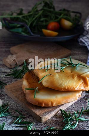 Geräucherte Provola-Medaillons auf Holzschneidebrett mit Kräutern und Gewürzen Stockfoto