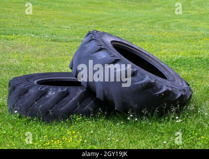 Zwei große abgenutzte schwarze Traktorreifen wurden auf einem grünen Rasen in Missouri aufgegeben. Bokeh-Effekt. Stockfoto