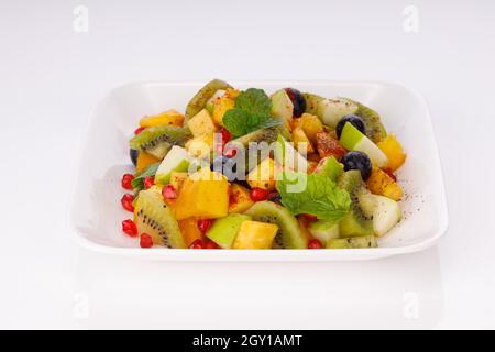 Gemischter Obstsalat in einem weißen Geschirr serviert und mit Minzblatt garniert. Stockfoto