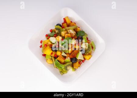 Gemischter Obstsalat in einem weißen Geschirr serviert und mit Minzblatt garniert. Stockfoto
