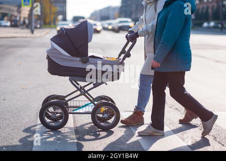 Beine von zwei Frauen mit Kinderwagen auf dem Fußgängerüberweg über die Straße Stockfoto