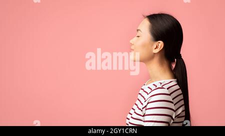 Profil Porträt Einer Jungen Ruhigen Asiatischen Frau Stehend Mit Geschlossenen Augen Über Rosa Hintergrund, Seitenansicht Aufnahme Einer Entspannten Friedlichen, Tausendjährigen Koreanischen Frau Stockfoto