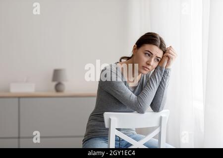 Traurig ängstlich frustriert Millennial Frau hat psychische Störungen, Probleme und schlechtes Gefühl, sitzt auf Stuhl allein Stockfoto