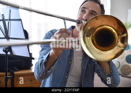 Detail des Posaunisten, der die Posaune im Wohnzimmer zu Hause übt. Vorderansicht. Horizontale Zusammensetzung. Stockfoto