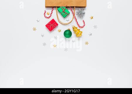 Weihnachten, Neujahr. Bastelpapierbeutel mit Geschenken, süßen Bonbons, Weihnachtsdekorationen, grünen Goldkugeln, silbernen Glitzer-Konfetti-Sternen auf weißem Hintergrund. Flach liegend, Kopierplatz Stockfoto