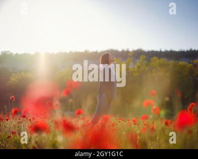 Junge schöne Frau mit erhobenen Armen im Frühjahr Mohnfeld. Sanfte Farben. Nachdenkliche, entspannte Atmosphäre. Stockfoto