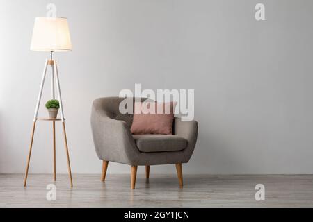 Bequemer Sessel mit rosa Kissen, leuchtende Lampe auf dem Boden auf grauem Wandhintergrund im Büro oder Wohnzimmer Stockfoto