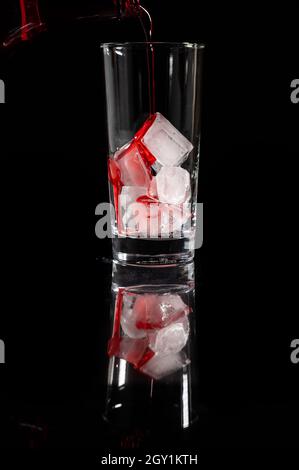 Gießen Sie rote alkoholfreie Lösung auf der Oberseite des Eises in das Glas vor komplett dunklem Hintergrund. Gießen Sie Alkohol, Weingut Konzept. Stockfoto