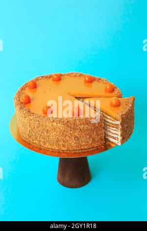 Geburtstagskuchen in Scheiben auf dem hölzernen Kuchenständer. Schöne Biskuitkuchen mit Physalis mit Schlagsahne verziert. Blauer Hintergrund. Speicherplatz kopieren. Essen pho Stockfoto