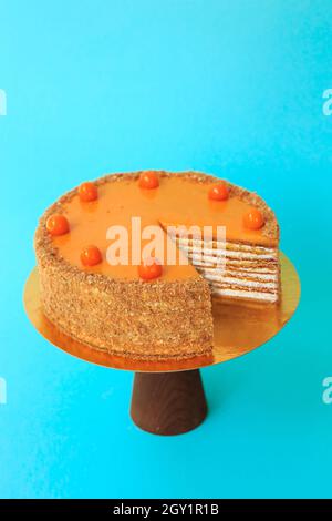 Geburtstagskuchen in Scheiben auf dem hölzernen Kuchenständer. Schöne Biskuitkuchen mit Physalis mit Schlagsahne verziert. Blauer Hintergrund. Speicherplatz kopieren. Essen pho Stockfoto