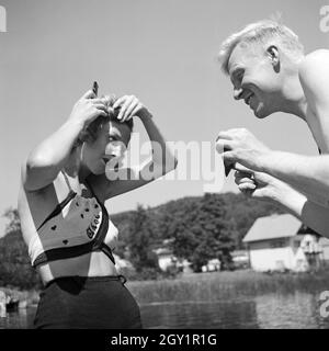 Ein junger Mann hält einer jungen Frau einen Spiegel, damit sie sich frisieren kann am Ufer eines sieht in der Wachau in Österreich, Deutschland, 1930er Jahre. Ein junger Mann hält einen Spiegel für eine junge Frau, die für ihre Frisur Check am Ufer eines Sees in der Wachau in Österreich, Deutschland 1930. Stockfoto