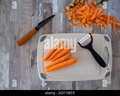 Karotten geschält auf dem Tisch liegend, neben einem Messer zum Schälen von Gemüse und Obst, Foto von oben, Lebensmittelkonzept Stockfoto