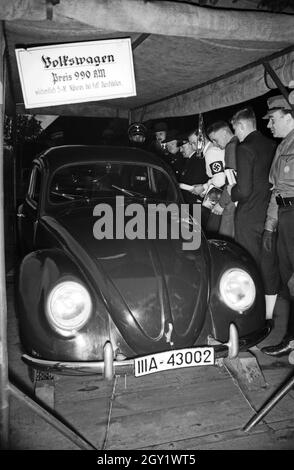 Ausstellungsbesucher informieren sich über die 'Sudetenfahrt der deutschen Technik' über die neuesten deutschen Erfahrungen auf dem Gebiet der Technik, hier präsentieren Nazifunktionäre den KdF Volkswagen, Deutschland 1930er Jahre. Besucher, die durch die Ausstellung der Propagandaausstellung "Sonderfahrt der deutschen Technik" gehen, präsentieren hier NAZO-Beamte den VW-Käfer, Deutschland 1930er Jahre. Stockfoto