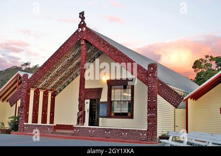 Ein traditionelles Maori Whare, oder Meeting House, in Rotorua, Neuseeland. Die Holzschnitzereien an der Außenseite des Versammlungshauses sind reich an Symbolik. Das Versammlungshaus ist ein Ort, an dem der Stamm und die Individuen gehört werden können, bekannt als tūrangawaewae. Die kulturelle Bedeutung des Versammlungsgebäudes an der Marae spiegelt sich in den Veranstaltungen wider, die dort stattfinden und von Gemeindeversammlungen bis hin zu Beerdigungen reichen. Stockfoto