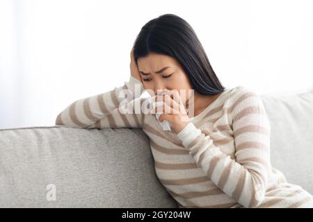 Saisonale Depression. Junge Asiatische Frau Weint, Während Sie Zu Hause Auf Der Couch Sitzt Stockfoto