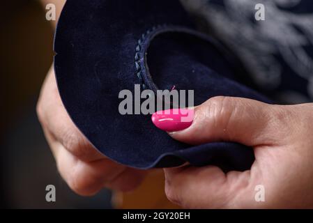 Frauenhänden nähen blaue Lederschuhe mit Nadel. Schuhmacher Werkstatt handwerklich handgefertigte Herstellung von Lederschuhen. Nahaufnahme Stockfoto