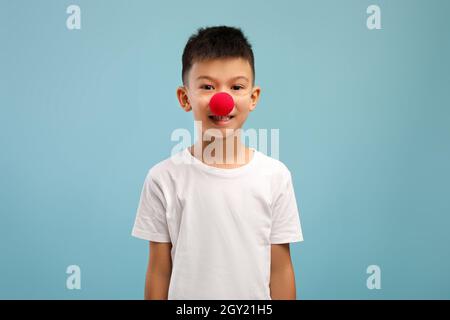 Lustiger kleiner asiatischer Junge, der die Nase des roten Clowns trägt und die Kamera anschaut Stockfoto