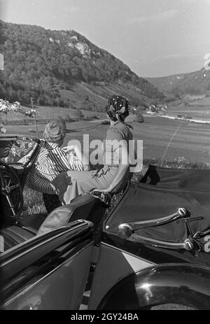 Zwei junge Frauen machen 5/6 einer Spazierfahrt mit dem Cabrio unter einem blühenden Kirschbaum im Schwarzwald Rast, Deutschland 1930er Jahre. Zwei junge Frauen ruhen unter einem blühenden Kirschbaum im Schwarzwald während Ihrer Reise mit einem Cabrio, Deutschland 1930. Stockfoto