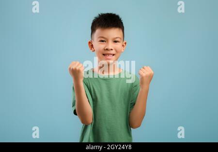 Ja. Überglücklich Kleiner Koreanischer Junge Schüttelt Die Fäuste Und Feiert Den Erfolg Über Blue Background Stockfoto