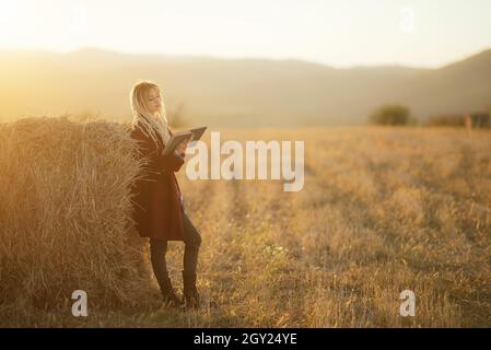 Hübsche junge Frau, die ein Buch auf dem landwirtschaftlichen Feld mit Heuhaufen liest Stockfoto