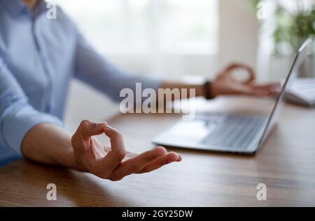 Nahaufnahme eines arabischen Mannes, der vor dem Laptop meditiert, Gyan Mudra macht, sich friedlich fühlt, am Arbeitsplatz Ruhe behält Stockfoto