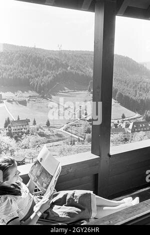 Eine junge Frau entspannt bei der Zeitschriftenlektüre auf dem Balkon, Freudenstadt, Deutschland 1930er Jahre. Eine junge Frau bei einem Magazin auf dem Balkon, Freudenstadt, Deutschland 1930. Stockfoto