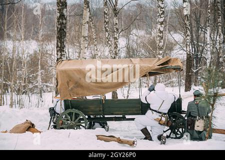 Hidden Re-enactor als deutscher Wehrmachts-Infanteriesoldat in World gekleidet Krieg II Soldaten sitzen in Hinterhalt in der Nähe von Bauernwagen in Winterwald Und Stockfoto