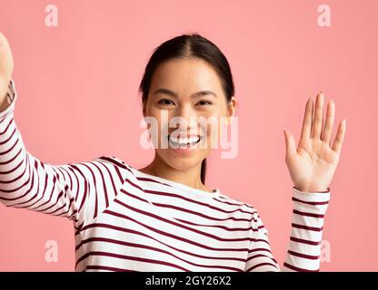 Hallo. Fröhliche Junge Asiatische Frau Nimmt Selfie Und Winkt Hand An Der Kamera Stockfoto
