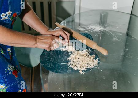 Eine unkenntliche Frau schneidet Nudeln. Frauenhände aus der Nähe. Stockfoto