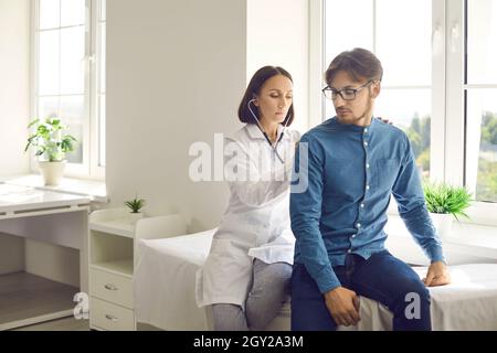 Arzt mit Stethoskop hört auf die Lungen eines jungen Patienten oder überprüft seinen Herzschlag Stockfoto