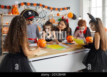 Gruppe von Kindern zusammen mit Frau bereitet handgemachte Halloween-Dekorationen aus Papier. Stockfoto