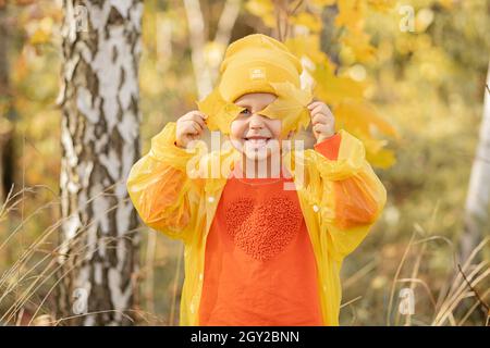 Foto von kleinen Mädchen von 5 Jahren ist glücklich, im Herbst zu frönen, zog sie auf gelben Hut und Regenmantel, geschlossenen Augen mit Herbstblättern von Bäumen Stockfoto