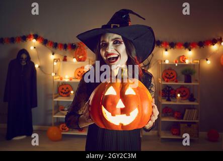 Halloween-Porträt der gruseligen und bösen Hexe mit glühenden Jack-o-Laterne in den Händen. Stockfoto