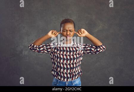 Launische junge afroamerikanische Frau bedeckt ihre Ohren mit den Fingern, um nichts zu hören. Stockfoto