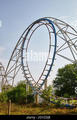 Zentrierte Aufnahme einer blauen Achterbahn, umgeben von Bäumen an einem klaren gräulichen Tag Stockfoto