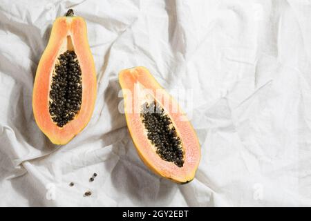 Kreatives Food-Konzept mit halber Papaya auf zerknittertem grauem Leinen. Flach Lay Draufsicht. Minimalistisch bunte Natur Hintergrund. Stockfoto
