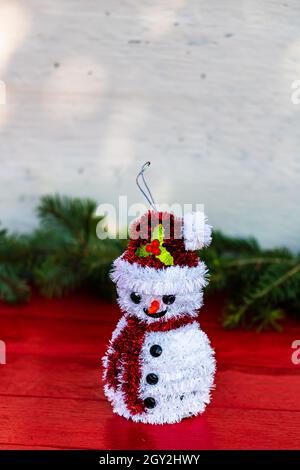 Vertikale Nahaufnahme eines Schneemann-Mockup auf einer roten Oberfläche mit einem Weihnachtsbaum-Blatt-Hintergrund Stockfoto