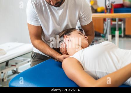 Nahaufnahme eines männlichen Physiotherapeuten, der eine junge kaukasische Patientin mit einer manuellen Halsdehnung begeht. Stockfoto