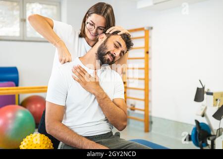 Frau Physiotherapeutin, die den verletzten Hals eines männlichen Patienten streckt. Stockfoto