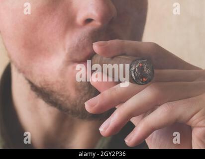 Ein Mann raucht eine kubanische Zigarre. Nahaufnahme der männlichen Hände mit einer rauchenden Zigarre aus Havanna Stockfoto