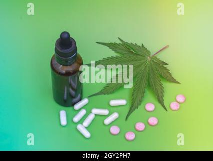 CBD-Pillen. Gruppe von CBD-Kapseln und rosa Cannabidiol-Pillen und Hanfblättern auf grünem Hintergrund. Verschiedene medizinische Cannabisprodukte. Medizinische Marijua Stockfoto