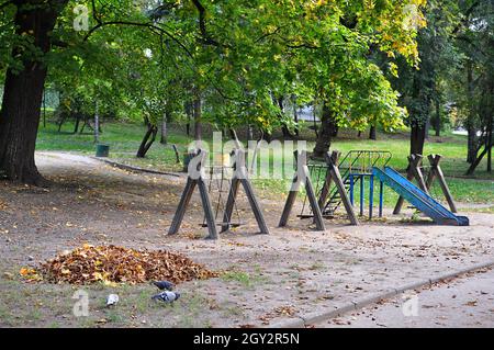 Alter und rostiger leerer Spielplatz im Stadtpark mit herbstlichen Blättern auf dem Boden Stockfoto