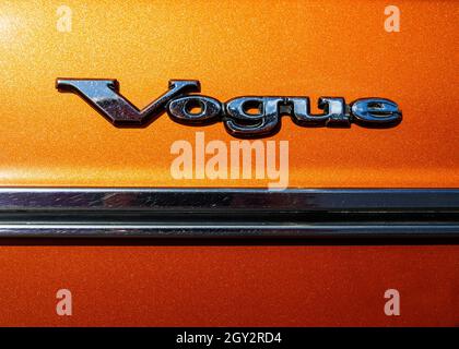 Abbildung des Chromabzeichens an der Seitentür eines Sunbeam Vogue-Autos aus den 1970er Jahren, das Wort Vogue über einem verchromten Türstreifen auf einer metallisch-orangenen Farbe Stockfoto