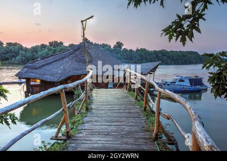 Schöner Sonnenuntergang im Sommer mit dem traditionellen rustikalen Restaurant auf dem Schlick Stara Koliba, an der Donau in Belgrad, Serbien. Stockfoto