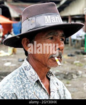 Ein Indonesier, der einen Marlboro Cowboyhut trägt und eine Zigarette raucht. Dies wurde auf einem Outdoor-Markt in Bukittinggi, West Sumatra, Indonesien, aufgenommen. Stockfoto
