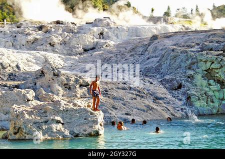 Maori schwimmen im blauen Wasser am Fuß des Pohutu Geyser in Rotorua, Neuseeland. Die Geyseritlandschaft wird während des Sommers für die Einheimischen zu einem Freiluftschwimmloch, wobei der Warmwasserschwimmbereich als „Blauen“ bezeichnet wird. Stockfoto