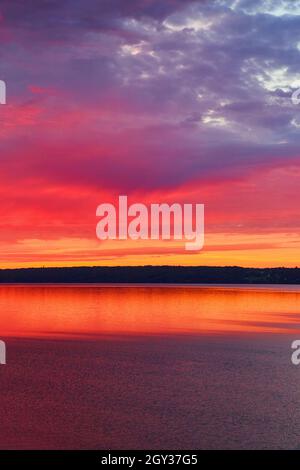 Lebhafter Sonnenuntergang in Rot, Orange und Violett über einem großen See Stockfoto