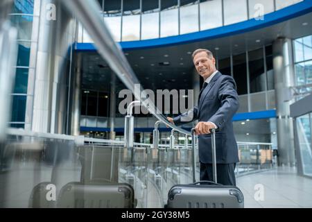 Lächelnder Geschäftsmann mit Koffer am Flughafen Stockfoto