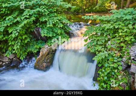 Kleiner Wasserfall über Trümmern mit grünen Büschen Stockfoto